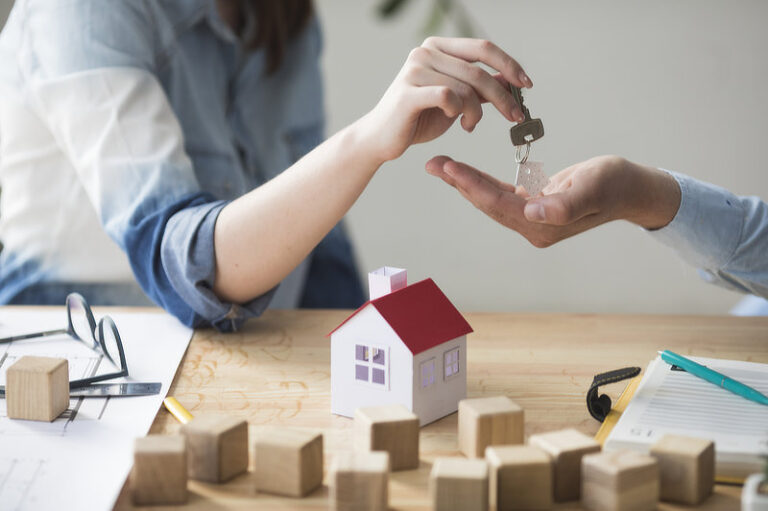 Woman's hand giving house key to man over wooden table.